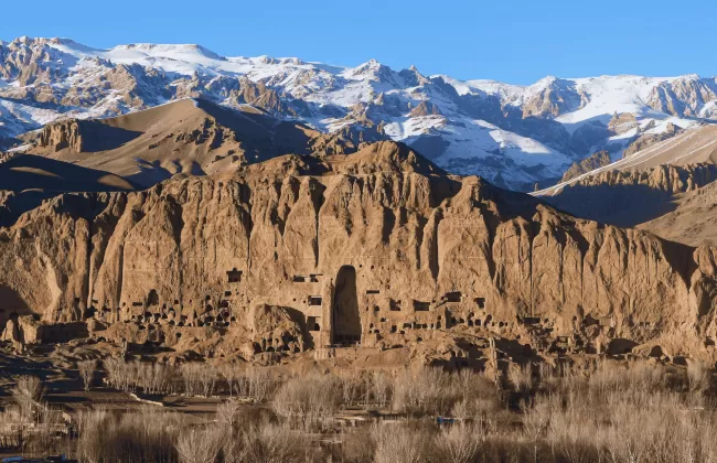Arid mountainous terrain with ancient ruins and snow-capped peaks in the distance.