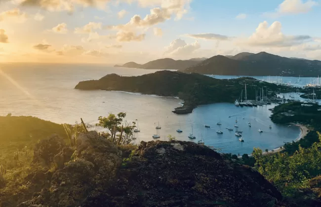 Sunset view of a tropical island coastline with boats anchored in a calm bay.