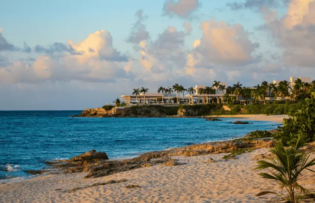 Peaceful tropical beach with turquoise waters and coastal villas under a colorful sky.