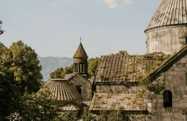 Ancient stone church surrounded by trees and mountains, typical of Armenian historical architecture.