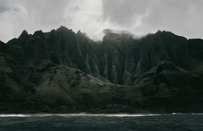 Dramatic dark green cliffs rising from the sea under moody clouds, showing the island's rugged beauty.