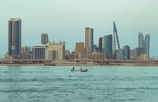 Modern skyline of Manama, Bahrain, with high-rise buildings viewed across the water.