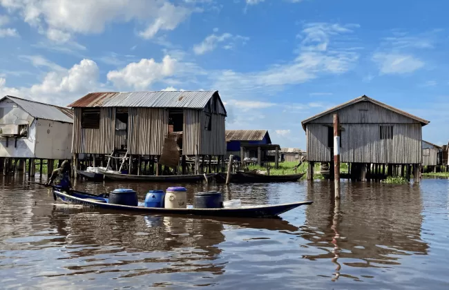 Traditional stilt houses and a boat on a calm waterway in a lakeside village in Benin.