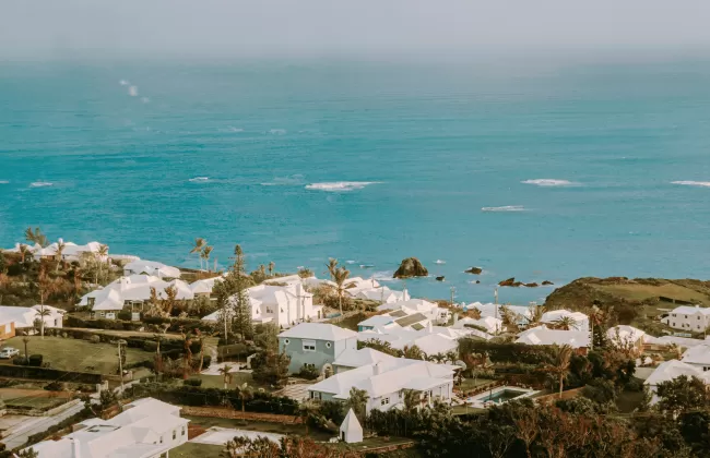 Coastal view of Bermuda with pastel houses and turquoise waters under a cloudy sky.