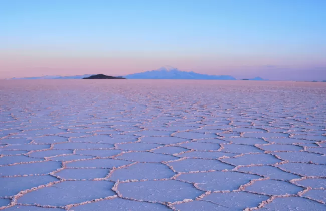 Expansive salt flats with hexagonal patterns stretching to the horizon under a pink and purple sky in Bolivia.
