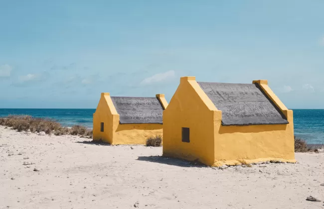 Two small yellow beach huts on a white sandy shore facing the turquoise sea in Bonaire.