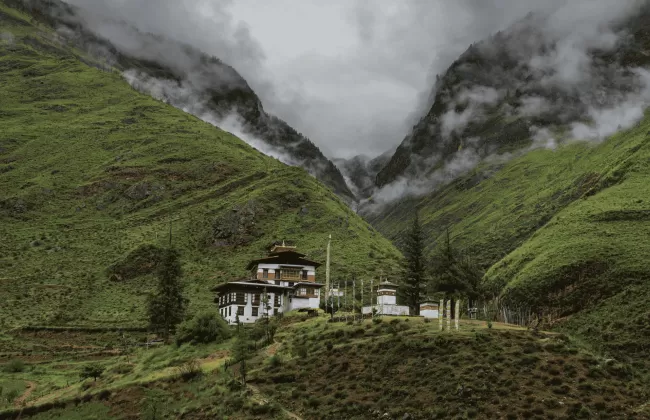 raditional building nestled in a lush, misty green valley surrounded by dramatic mountain peaks in Bhutan.