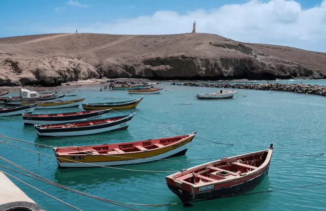 Traditional fishing boats moored in a calm bay with arid hills in the background in Cape Verde.