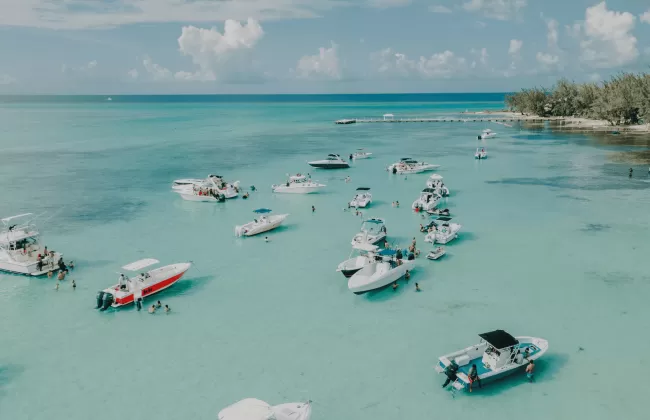 Boats floating on crystal-clear turquoise water near a white sandy coast in the Cayman Islands.