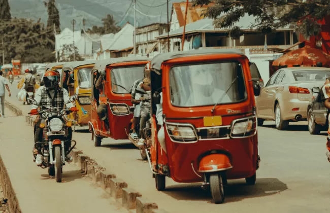 A lively street with red tuk-tuks, people walking, and shops along the roadside.