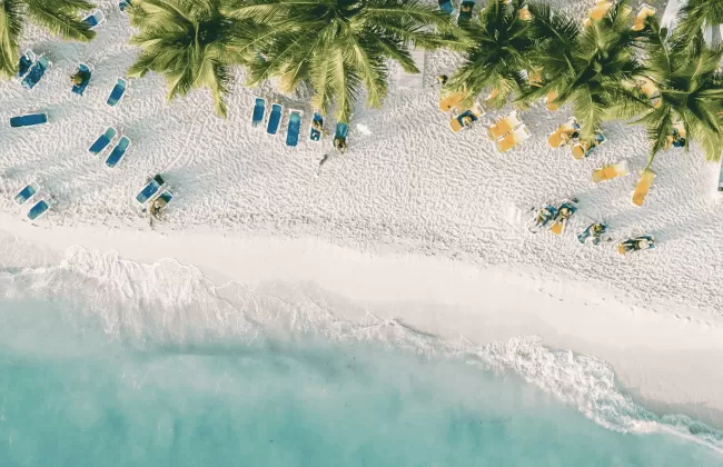 A white sandy beach with turquoise water and lush green trees along the shoreline.