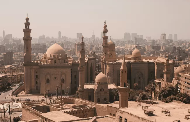 A historic cityscape with mosques, minarets, and sandy-colored buildings.