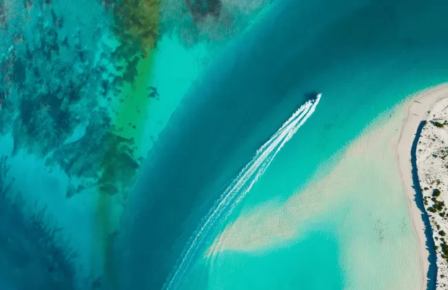 Aerial view of a tropical shoreline with turquoise waters and a speedboat.