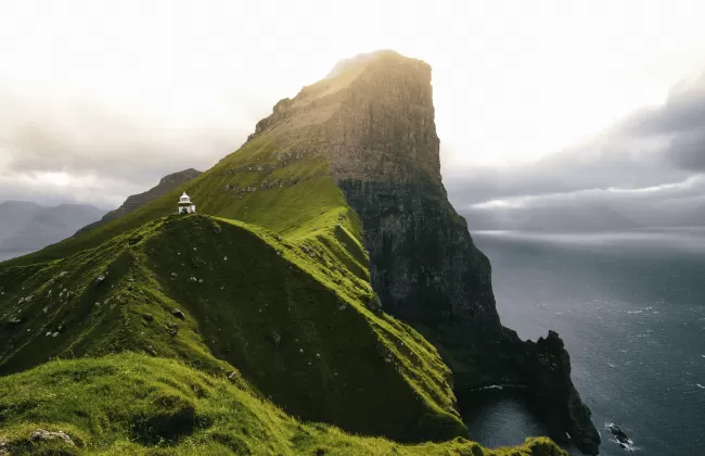 Steep green cliffs rising from the ocean with fog in the background.
