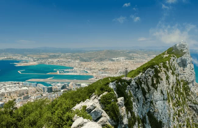 A rocky cliffside with ocean views and a distant town.