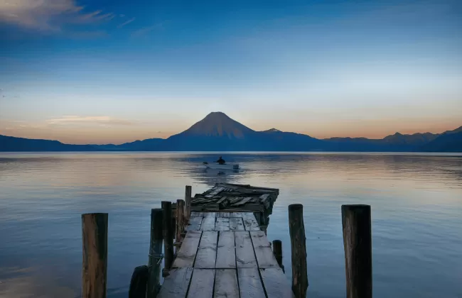 A wooden pier extending into calm waters with a mountain in the distance.