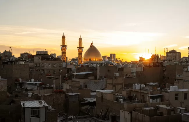 A sunset over Baghdad, Iraq, with mosque minarets silhouetted against the sky.