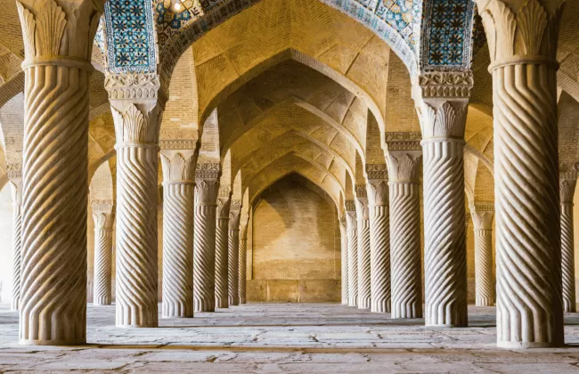The interior of a historic Persian mosque in Iran with intricate arches and tiles.
