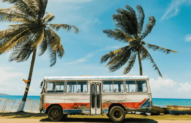 A colorful bus parked under palm trees on a tropical beach in Jamaica.