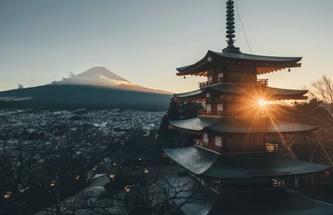 A traditional Japanese pagoda with Mount Fuji in the background during sunset.