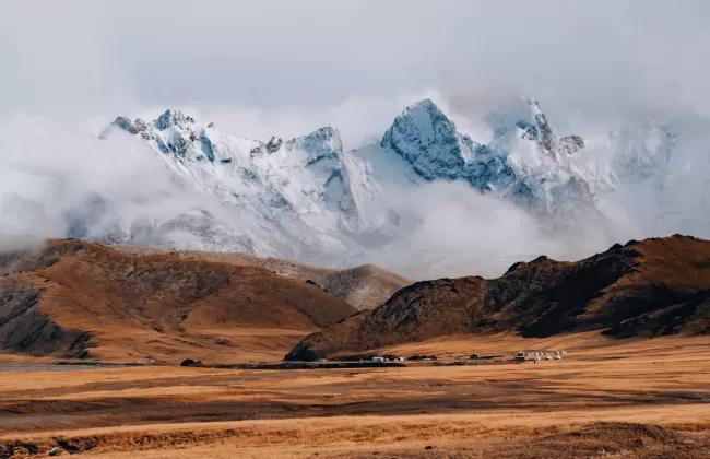 Snow-capped mountains rise over a dry, golden plain in Kyrgyzstan.