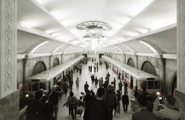A large metro station hall with chandeliers and people walking.