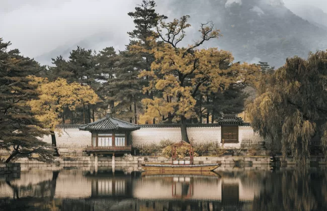 Traditional temple buildings by a calm reflective pond surrounded by trees.