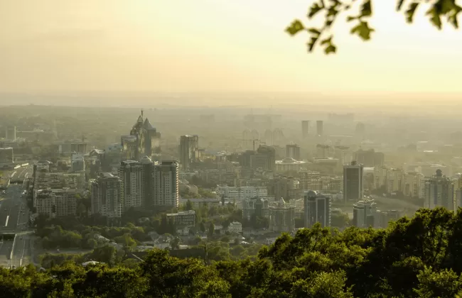 A hazy cityscape of Almaty, Kazakhstan, with buildings surrounded by greenery.