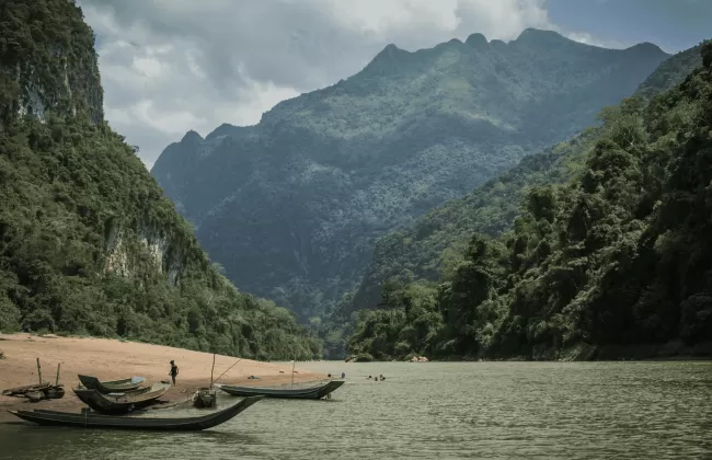 A tranquil river in a lush green valley surrounded by forested mountains, with a traditional boat on the water.