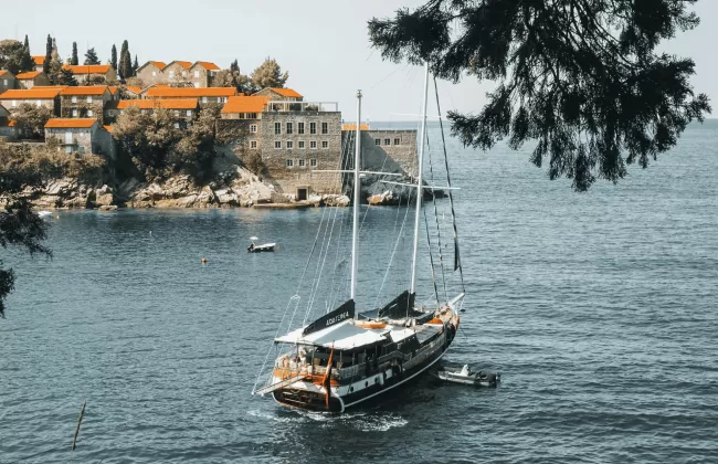 Coastline with cliffs, greenery, and a sailing boat.