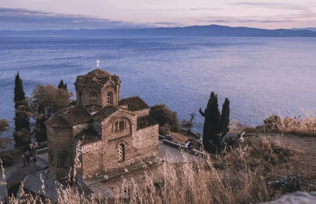 Ancient stone ruins and a church on a hillside with mountains behind.