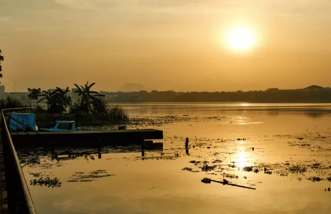 A golden sunset over a wide river with scattered boats and trees.