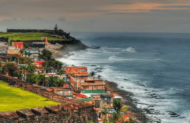 Colorful houses on a hillside by the ocean with waves crashing on the shore.
