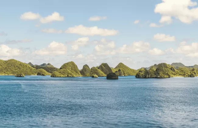 A group of small green islands surrounded by bright blue tropical water.