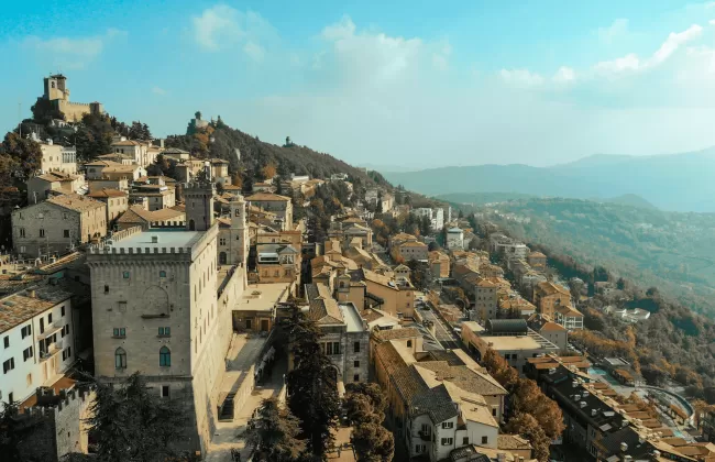 A hillside town with stone buildings and mountains in the distance.