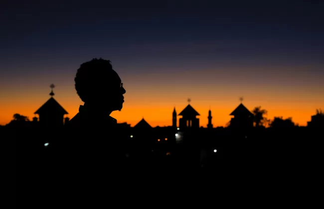 Silhouettes of trees and a person against a deep orange sunset sky.