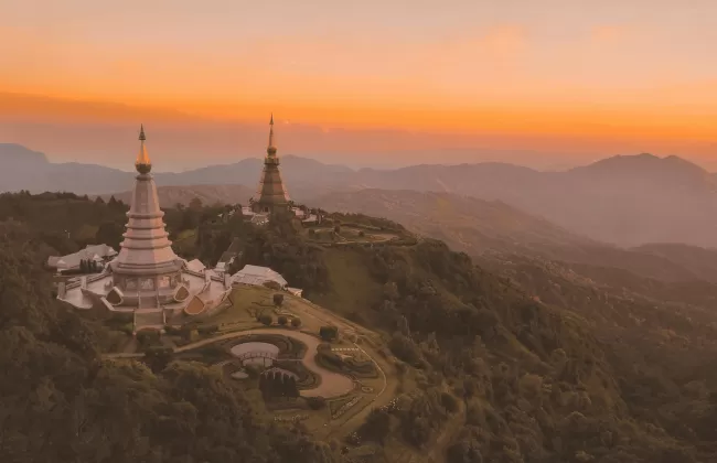 Twin golden pagodas on a hilltop surrounded by forests at sunset.