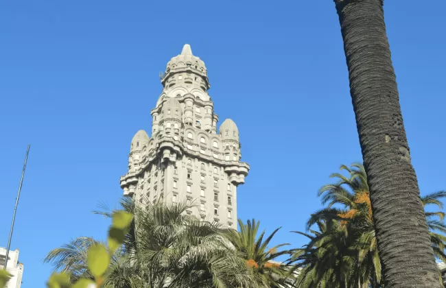 Historic building with intricate tower and palm trees against a blue sky.