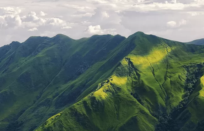 Lush green mountains covered in sharp ridges under cloudy skies.