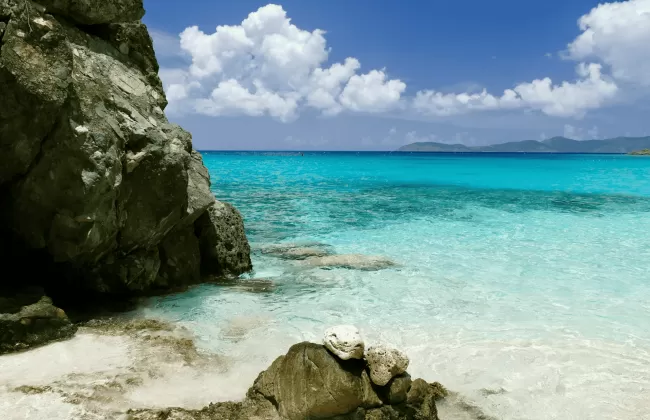 Rocky tropical shoreline with turquoise waters and white sand.