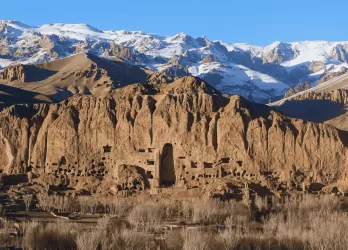 Arid mountainous terrain with ancient ruins and snow-capped peaks in the distance.