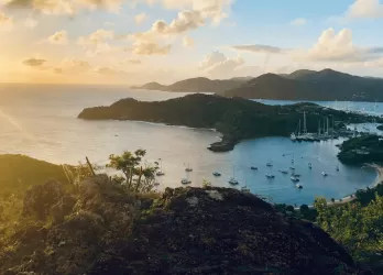 Sunset view of a tropical island coastline with boats anchored in a calm bay.