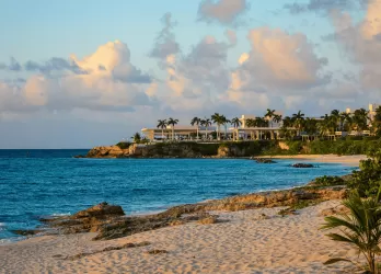 Peaceful tropical beach with turquoise waters and coastal villas under a colorful sky.
