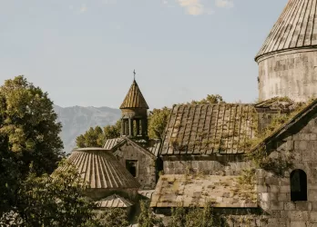 Ancient stone church surrounded by trees and mountains, typical of Armenian historical architecture.