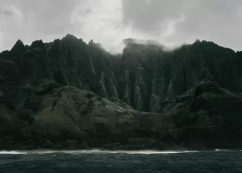 Dramatic dark green cliffs rising from the sea under moody clouds, showing the island's rugged beauty.