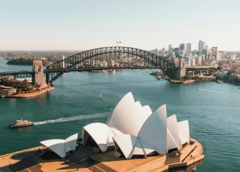 Aerial view of Sydney Harbour with the Sydney Opera House and Harbour Bridge under a clear sky.