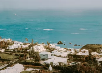 Coastal view of Bermuda with pastel houses and turquoise waters under a cloudy sky.