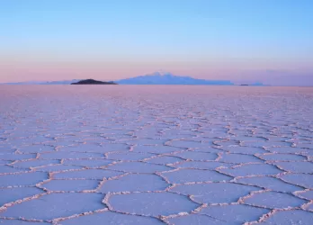 Expansive salt flats with hexagonal patterns stretching to the horizon under a pink and purple sky in Bolivia.
