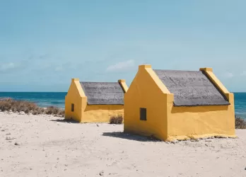 Two small yellow beach huts on a white sandy shore facing the turquoise sea in Bonaire.