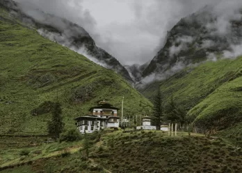 raditional building nestled in a lush, misty green valley surrounded by dramatic mountain peaks in Bhutan.